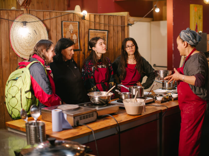 Woman teaching four women to cook in wood-panelled kitchen